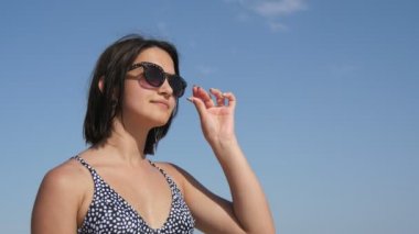 Güzel kız güneş gözlüklerini çıkarır ve yaz aylarında tatil köyünde baş aşağı yatar. Bikini giyen, güneş gözlüğünü çıkartan ve güneşli bir yaz gününde deniz kıyısında tatil yapan çekici esmer bir kızın ilham verici manzarası..