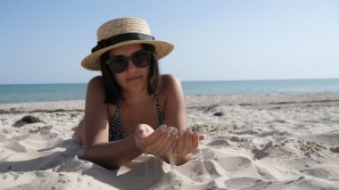 Güneş gözlüklü ve bikinili gülümseyen kız Karadeniz kıyısında ağır çekimde yatıyordu. Bikini giyen, saman şapkalı ve güneş gözlüklü, kumlu sahilde uzanmış, kumları alıp yavaş çekimde Karadeniz kıyısına dökülen esmer kız heyacanlı bir manzaraydı.