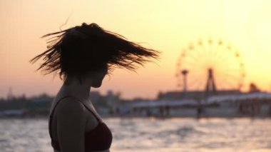 Muhteşem bir şehir iskelede kafasını sallıyor yavaş çekimde muhteşem bir gün batımında. Bikinili güzel bir esmer kızın ıslak saçlarını altın rengi günbatımında dönme dolaba sallamasını etkileyici bir şekilde görüyoruz.