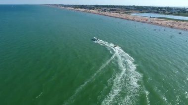 Yazın açık denizde, güneşli bir yaz gününde mutlu turistlerle dolu hızlı beyaz sürat teknesinin şişme halkasının iyimser görüntüsü ile modern motorlu tekne çekme halkasının hava görüntüsü. Tekne yavaş yavaş sola dönüyor..