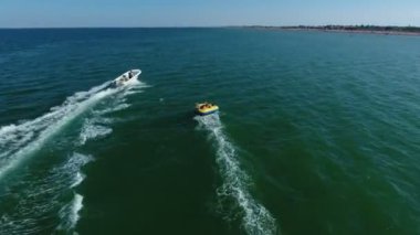 Yazın açık denizde neşeli turistlerle halkayı çeken büyük teknenin havadan çekilmiş görüntüsü. Güneşli bir yaz gününde neşeli insanlarla dolu şişme halkayı çeken büyük beyaz bir motorlu teknenin muhteşem görüntüsü. Yüzük yılan gibi hareket ediyor..