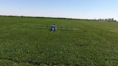 Büyük yeşil pirinç arazisinin havadan çekilmiş görüntüsü ve yazın püskürtülen bir traktör ile güneşli bir günde yeşil pirinç bölgesinde sulama kanalları boyunca hareket eden büyük bir traktörün muhteşem kuş bakışı görüntüsü..  