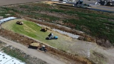 Yazın büyük tarım deposuna yeşil silo döken hareket halindeki kamyonun havadan çekilmiş görüntüsü güneşli bir yaz gününde iki buldozerle birlikte açık tarım deposuna eğimli kutusundan yeşil silo atan hareket halindeki bir kamyonun görüntüsü. Güzel görünüyor..
