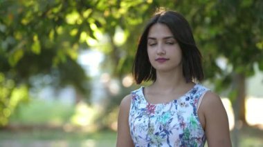 Güneşli bir günde yeşil parkta ayakta duran ve siyah maske takan güzel esmer kız. Yeşil parkta koronavirüsten korunmak için bale maskesi takan çekici, ince ve güzel esmer kız manzarası.