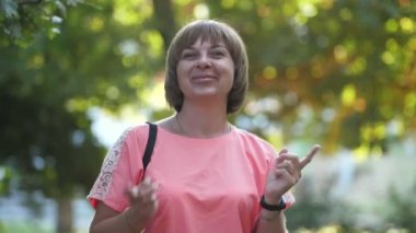 Yazın yeşil bir parkta neşeli bir şekilde dans eden mutlu sarışın kadın. Kısa saçlı, kısa saçlı, pembe elbiseli, neşeli bir kadın. Yavaş çekimde yeşil ve güneşli park alanında dans eden bir disko..