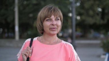 Hafif elbiseli çekici bir kadın yazın ağır çekimde rıhtımda gülümsüyor ve ayakta duruyor. Yazın güneşli bir yaz gününde siyah bir çantayla gülümseyen ve Dinyeper nehir kıyısında ayakta duran mutlu sarışın bir kadının ilham verici görüntüsü. 