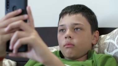 Dinlenen bir çocuk, havadar bir apartman dairesinde, yeşil tişörtlü, kısa saçlı, gevşetici esmer bir çocuğun, havadar bir dairede, akıllı telefonunda yalan söyleyip video oyunları oynaması alışılmadık bir manzara.. 
