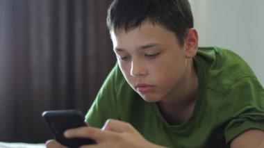 Akıllı bir adam kanepede oturup akıllı telefonuyla video oyunu oynuyor. Evinde, kısa saçlı, kısa saçlı ve şortlu akıllı bir esmer çocuk oturuyor. Kanepesinde oturuyor ve telefonunda video oyunu oynuyor.. 