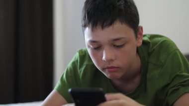 Kanepede oturan ve akıllı telefonuyla video oyunlarının keyfini çıkaran nişanlı bir çocuk. Kısa saçlı, kısa saçlı, kanepede oturan ve telefonundaki video oyununun keyfini çıkaran zeki bir esmer çocuk.. 