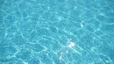 Açık mavi dalgalar, yavaş çekimde temiz sularda, kristal bir yüzme havuzunda kristal bir çakıl taşıyla yavaşça sallanan mavi seleste dalgalarının büyüleyici görüntüsüyle hafifçe hareket ediyor..