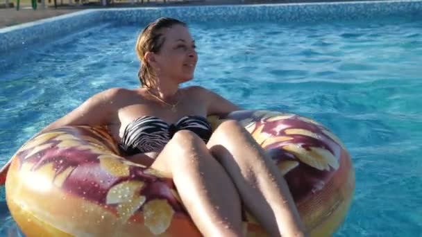 熱狂的なブロンド女性笑顔と座っていますカラフルな水チューブでSlo Moビビット座っています 笑顔とターンアウトオンA水ダウンでA Wading Poolで輝く水とともに夏にスローモーション — ストック動画