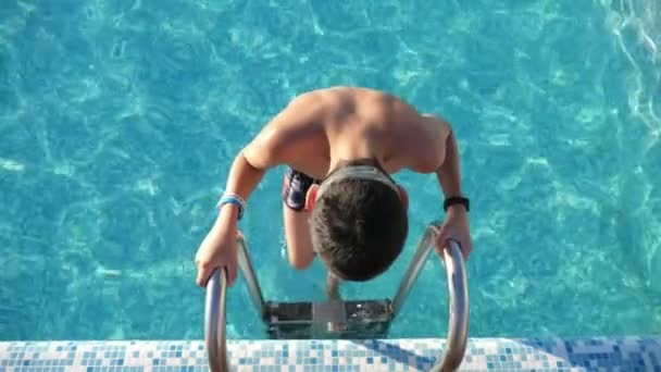 브루넷 소년이 동작으로 수영장에서 사다리를 내려가는 모습은 가래와 반바지를 금속으로 — 비디오