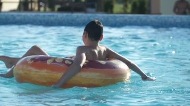 Mutlu çocuk su halkasının üzerinde oturuyor ve annesi onu yavaş çekimde gülümseyen esmer bir çocuğun neşeli görüntüsüyle büyük bir su tabancasında otururken annesi onu yazın ağır çekimde köpüklü suyla yüzme havuzunda döndürüyor.