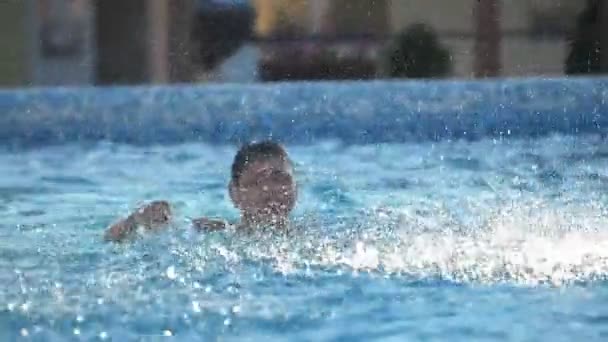 快乐的男孩用手滑水 慢动作时滑落了许多水滴 快乐的男孩看到一个快乐的黑发男孩在水里玩耍 用手滑水 夏天在游泳池里喷出数千个闪闪发光的水花 — 图库视频影像