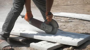 İnşaat işçisi güneşli bir günde beton bir plakayı disk öğütücüyle kesiyor. Üniformalı bir adamın etkileyici bir şekilde yakın plan çekimini sürdürüp güneşli bir yaz gününde inşaat alanında beton bir plakayı iki parçaya bölüyor.