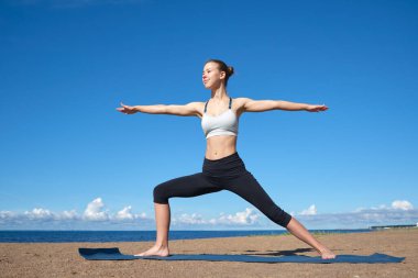 Genç sıska kız güneşli bir sabahta sahilde yoga yapıyor.