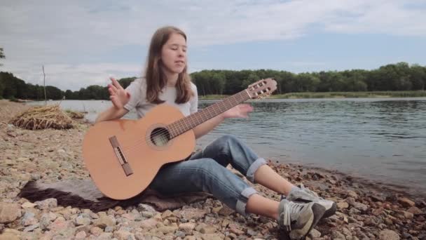 Jong meisje leert gitaar spelen in de natuur in de buurt van een prachtig meer, hobby concept — Stockvideo