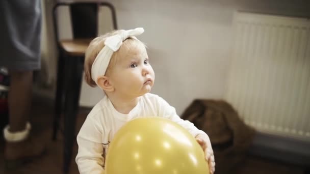 Niña de un año mira a mamá sostiene en sus manos un globo amarillo — Vídeo de stock