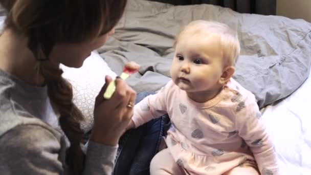 Young mother feeds infant baby daughter with a spoon — Stock Video