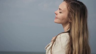 young happy woman with long hair in a beige coat close-up dancing on the sea beach
