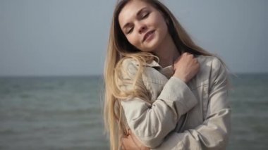young happy woman with long hair in a beige coat close-up dancing on the sea beach
