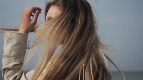 Mujer joven en un impermeable bailando en la playa del mar, caminando por la costa — Vídeo de stock