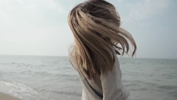 Молодая женщина в дождевике танцует на берегу моря, гуляет по побережью — стоковое видео