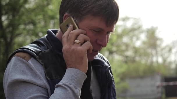 Un hombre de mediana edad de unos 50 años está hablando por teléfono afuera en un parque — Vídeo de stock