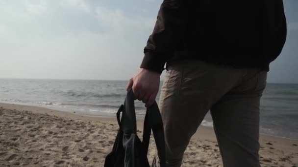 Anak muda 20 tahun berjalan di sepanjang pantai Laut Baltik dengan ransel di tangannya — Stok Video