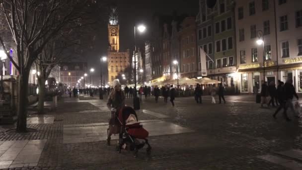 Молода жінка носила доньку в червоному візку вночі в Гданську Польщу. — стокове відео
