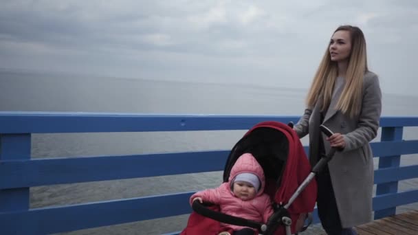 Mladá matka žena kráčí podél nábřeží s kočárkem, ve kterém je holčička dcerou — Stock video