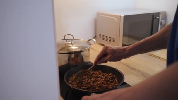 Jonge man koken in de keuken spaghetti Bolognese frietjes gehakt met saus in een pan — Stockvideo