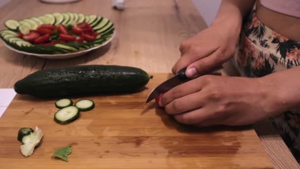 Mujer corta verduras en una tabla de madera con un cuchillo de cerca, tomates y pepinos — Vídeos de Stock