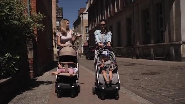 Unga lyckliga mödrar kvinnor med barnvagnar gå ner på gatan talande promenad — Stockvideo