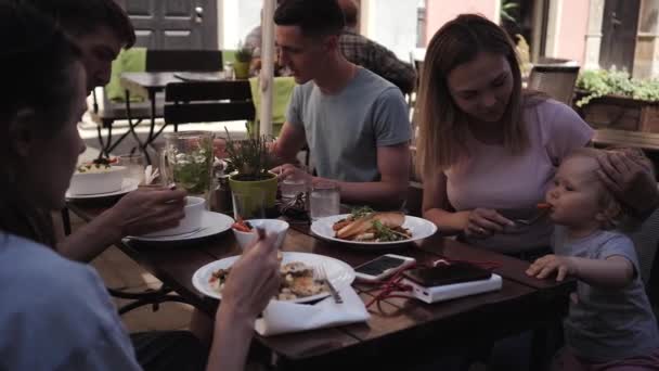 Группа молодых людей с детьми обедают в кафе на улице — стоковое видео