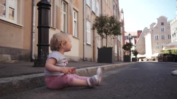 Kleines blondes, lockiges Mädchen, das auf der Straße sitzt und die Straße hinunterläuft — Stockvideo