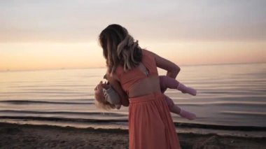 Anne ve kızı gün batımı gülüyor deniz kıyısında yürümek 