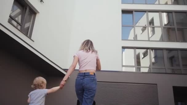 Jonge moeder wandelingen met haar dochter rond het huis reist wandelen langs de straat — Stockvideo