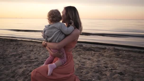 Mãe e filha caminham ao longo da praia ao pôr do sol rindo — Vídeo de Stock