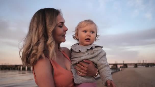Moeder en dochter lopen langs de kust bij zonsondergang lachen — Stockvideo