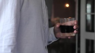 Beyaz gömlekli genç adamların elinde bir bardak viski suyu.