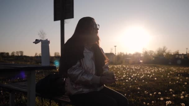 Jonge vrouw met bril genieten van het drinken van warme thee buiten kijken naar de zonsondergang — Stockvideo