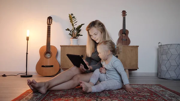 Genç anne ve kız yerde oturup video bağlantısıyla konuşuyorlar.