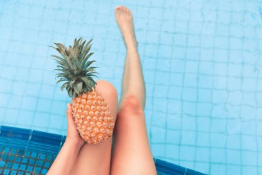 Yaz kavramı, kadın el ananas tutarak ve bacaklar yüzme havuzunda rahatlatıcı.