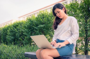 Dizüstü bilgisayar kullanarak ve Bahçe bankta oturan genç kadın portresi.
