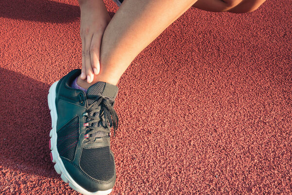 Close up portrait of sporty woman having ankle injury in running track., Healthcare and sport concept.