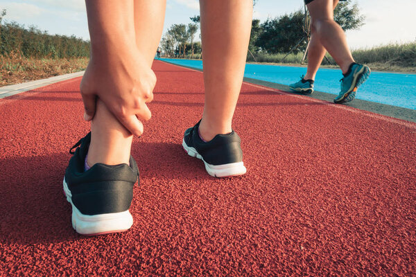 Close up portrait of sporty woman having ankle injury in running track., Healthcare and sport concept.