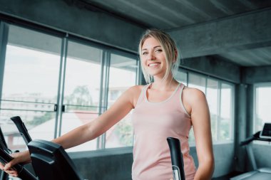 Kadın egzersiz eliptik eğitmen egzersiz fitness spor salonunda, oldukça çekici beyaz kadının yapması portresi eliptik eğitmen kapalı spor salonunda, spor egzersiz sırasında gülümseyen güzel kız.