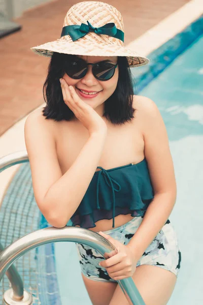 Portrait of beautiful woman relaxing in swimming pool, Recreation sport outdoor and summer vacation., Pretty woman in swimsuit with her hat relaxing sunbathing beside poolside. Summer holiday concept.