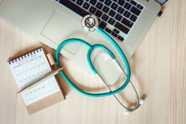 İş Sağlık Tıp ve sigorta Concept.Top görünümünü stetoskop ile takvim check-up kavramı., yıllık doktor randevu ahşap arka plan karşı fiziksel Check-Up için bir laptop